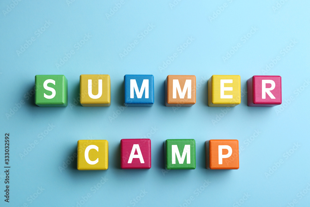 Colorful wooden cubes with phrase SUMMER CAMP on light blue background, flat lay