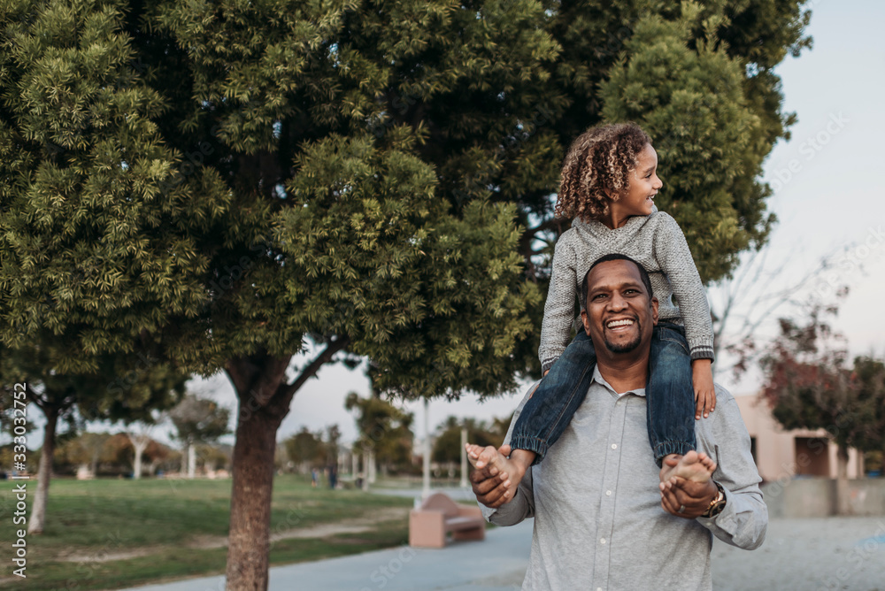 Joyful son sitting on a happy father's shoulders at park playground Joyful son sitting on a happy father's shoulders at park playground