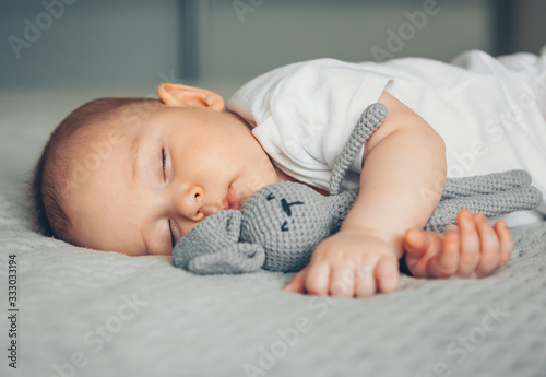 Sweet newborn baby sleeps with a gray toy hare