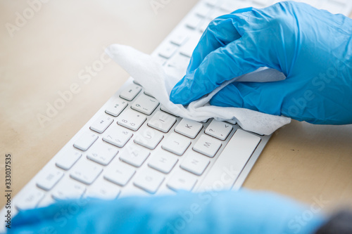 Coronavirus Epidemic Outbreak. Close-up of hand in protective glove using wet wipe to disinfect a computer keyboard. 
