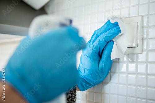 Coronavirus Epidemic Outbreak. Close-up of hand in protective glove using wet wipe to disinfect a switch. 