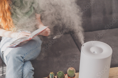 Household humidifier at home on table near woman reading on sofa photo