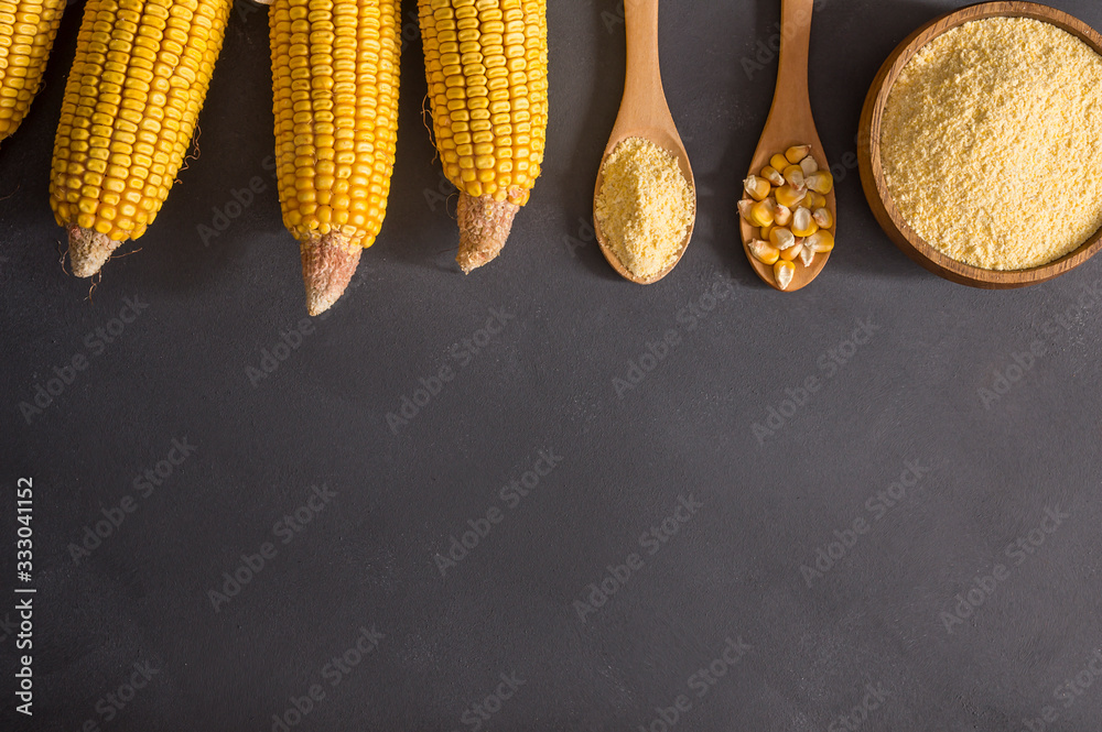 Corn flour in wooden bowl and spoon with dried corn groats, kernels on