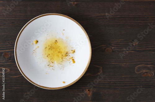 Food leftovers after meal. Yellow fat with spices on a single white plate. Wooden table background. Top down flat photo with copy space