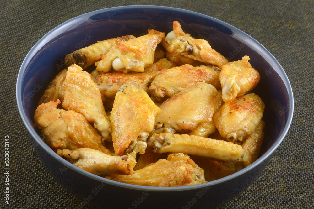 Golden brown baked chicken wings in large blue bowl on table Golden brown baked chicken wings in large blue bowl on table