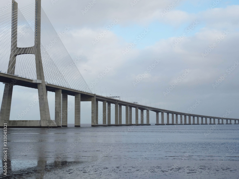 Bridge Vasco de Gama Lisbon crossing the river Tejo reflected in the water on a cloudy day. Bridge Vasco de Gama Lisbon crossing the river Tejo reflected in the water on a cloudy day.