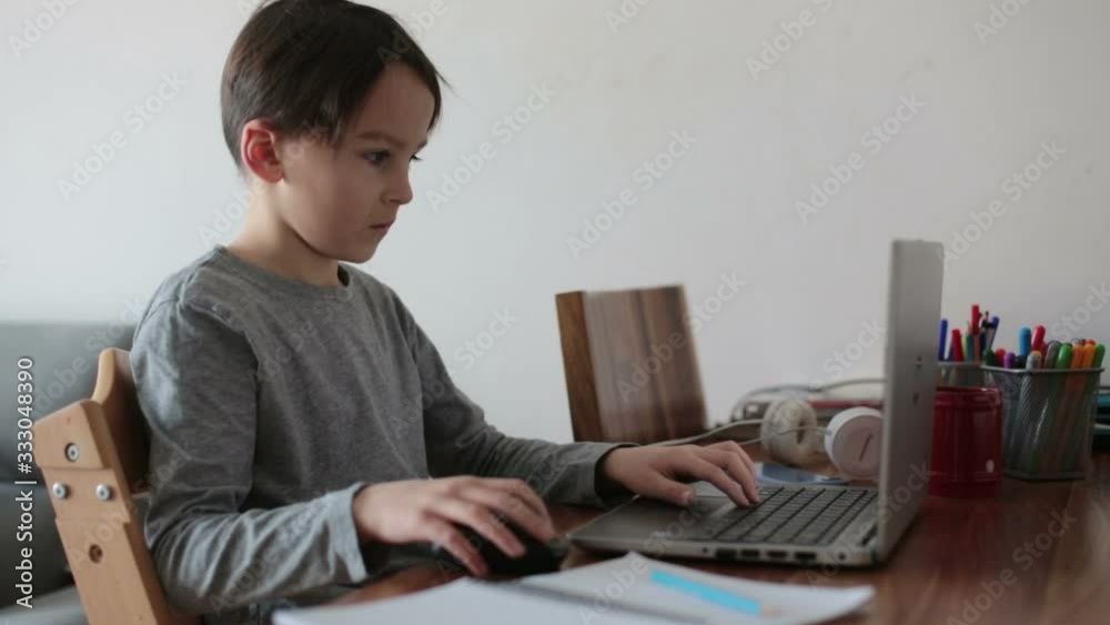School child, sitting at the table with laptop, writing school tasks while homeschooling, while school closed due to Coronavirus School child, sitting at the table with laptop, writing school tasks while homeschooling, while school closed due to Coronavirus