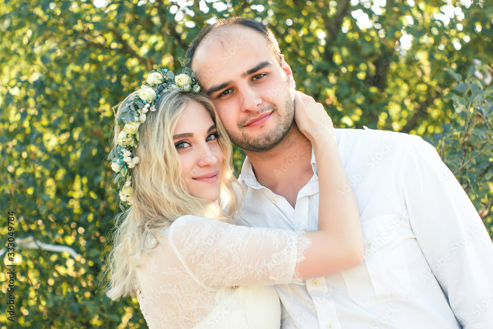 Bride in white dress and wreath and groom portrait in sunny summer day. Rustic outdoor wedding concept. Soft focus. Bride in white dress and wreath and groom portrait in sunny summer day. Rustic outdoor wedding concept. Soft focus.