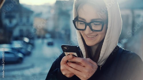 Wallpaper Mural Close up view of attractive caucasian stylish woman in white hoodie and black modern glasses use smartphone smiling feeling happy having fun texting message scrolling tapping Sunny day spring outdoor Torontodigital.ca