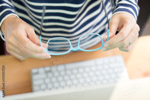 Closeup, hands of woman hold eyeglasses in front of computer due to eyestrain and headache from working and looking at digital screen for long period of time. Computer vision syndrome problem concept. photo