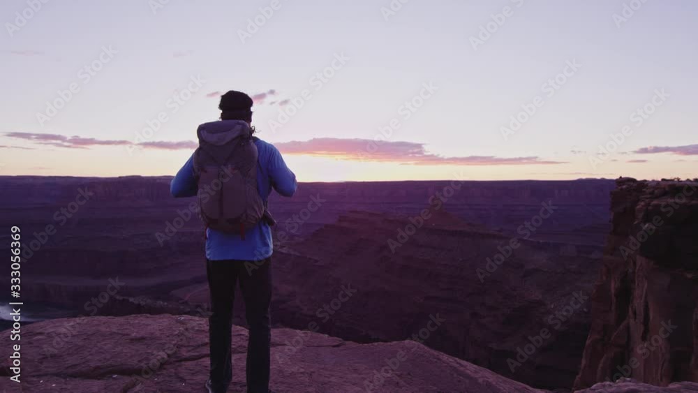 Hiker with Backpack walks to cliff edge and overlooks canyon