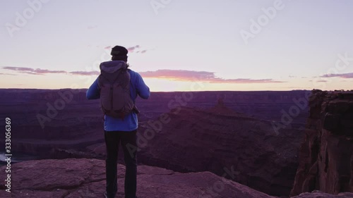 Hiker with Backpack walks to cliff edge and overlooks canyon