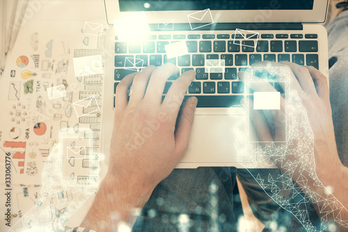 Double exposure of man's hands typing over computer keyboard and flying envelop hologram drawing. Top view. e-mail concept.