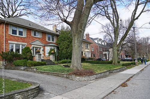 Residential street with large detached houses with front yards with mature trees