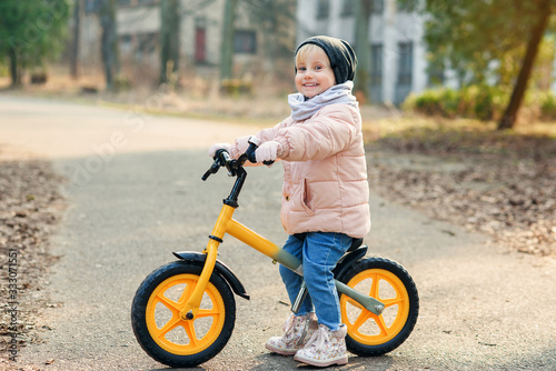 Fototapeta Naklejka Na Ścianę i Meble -  Baby girl rides a bicycle outdoors at the park. Little kid enjoying a happy childhood at warm spring day.