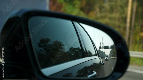 Close-up Side-view mirror Reflection Car Moving Behind Following on Highway. Bright Sunny Summer Autumn Morning Day, Blue Sky. 2x Slow motion 0.5 speed 60 FPS