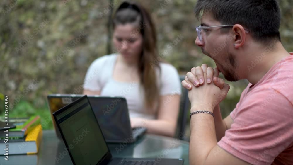 Closeup on college boy in focus and high school teen girl doing school work on their laptops outside while on lock down from coronavirus. Closeup on college boy in focus and high school teen girl doing school work on their laptops outside while on lock down from coronavirus.