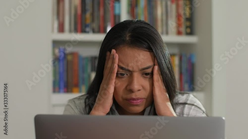 Close-up of a Hispanic or Asian woman is sitting at home in front of a laptop computer, being worried, fearful and frustrated