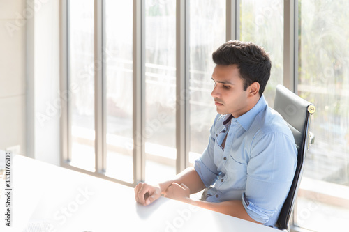 An Indian handsome man wearing a blue shirt sitting in his office in the office in the morning. He has a sad face because of concerns that his startup may have to close down the business.