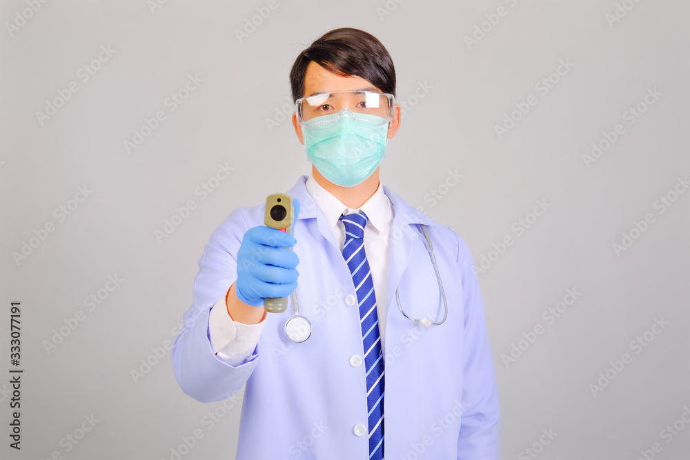 Medical doctor in white uniform doctor wears medical gloves, medical masks and and wearing protective glasses holding infrared forhead thermometer on gray background, corona virus concept Medical doctor in white uniform doctor wears medical gloves, medical masks and and wearing protective glasses holding infrared forhead thermometer on gray background, corona virus concept