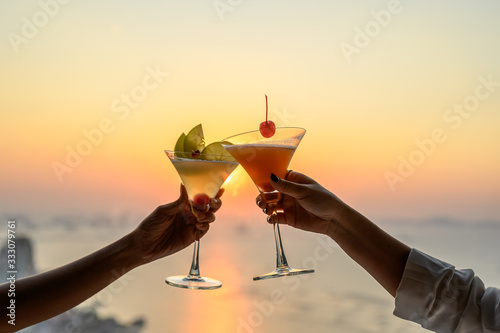 Fotografia Couple enjoying of Cheers glass of cocktail in a restaurant  at sunset view sea