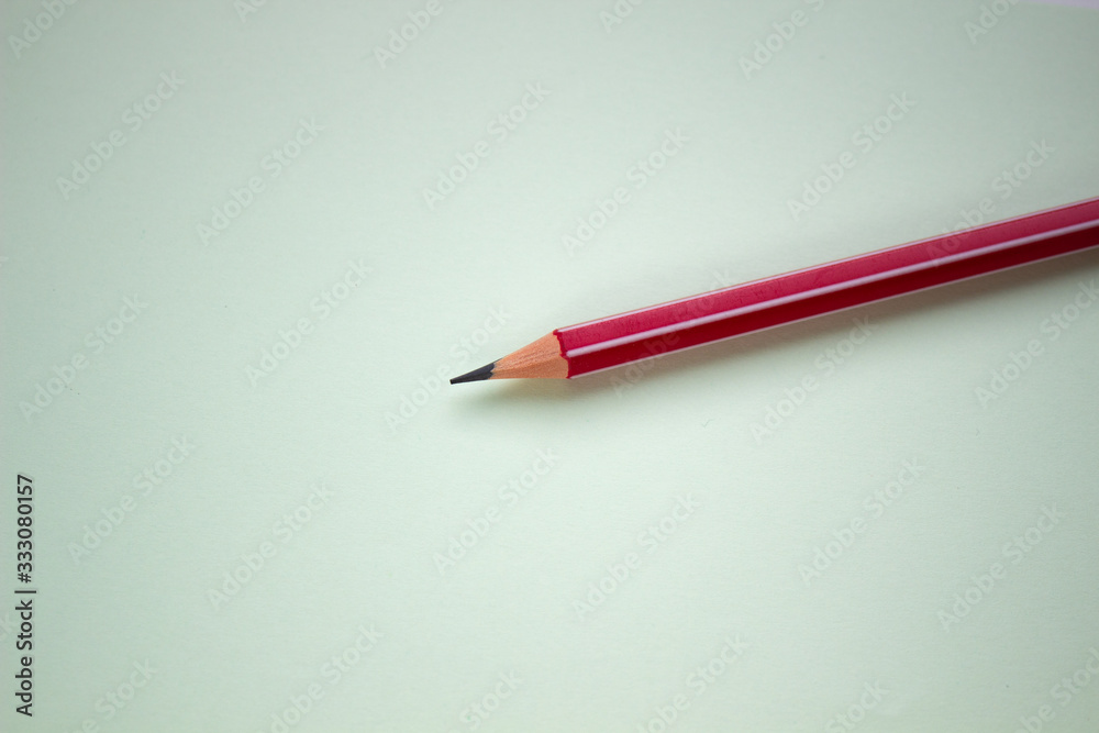 One red pencil on a light green background.