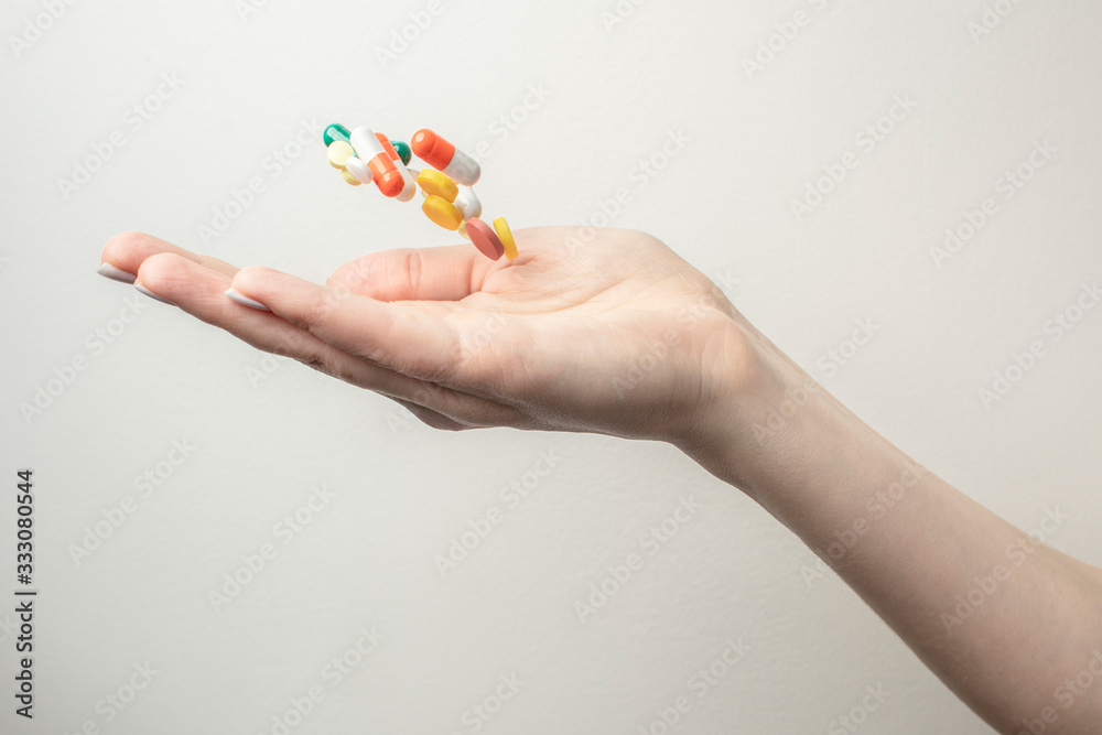 A lot of different pills falling into woman's hands. Drugs against the COVID-19 and other conditions and diseases on the white background. A lot of different pills falling into woman's hands. Drugs against the COVID-19 and other conditions and diseases on the white background.