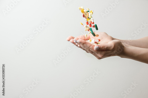 A lot of different pills falling into woman's hands. Drugs against the COVID-19 and other conditions and diseases on the white background.