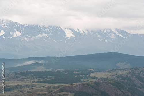 snow peaks on horizon, ridge of rocks under cloudy sky in mountain valley © Koirill