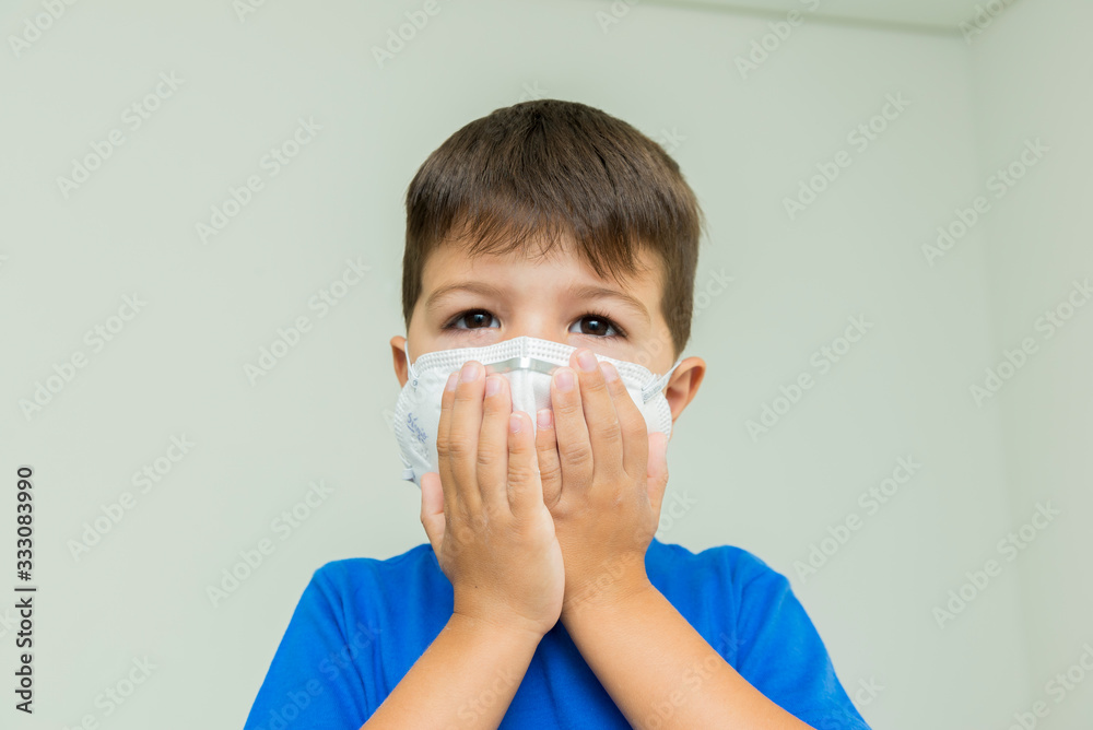 Caucasian boy with surgical mask with hands on his face and scared.