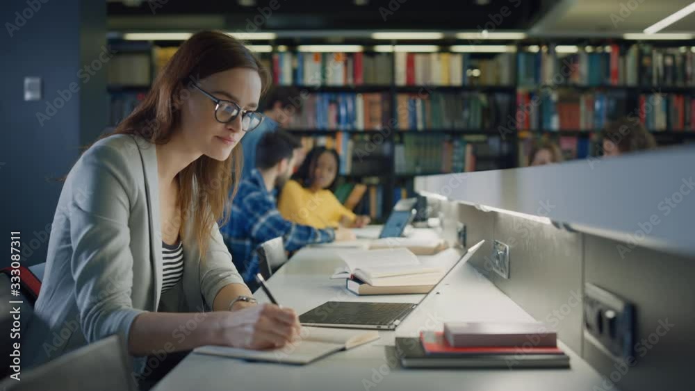 University Library: Talented Caucasian Girl uses Laptop, Smart Helpful Classmate Explains and Advices Her with Class Assignment. Happy Diverse Students Talking, Learning, Studying Together for Exams