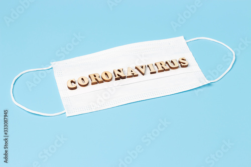 Inscription coronavirus made of wooden letters on white mask on a blue background.