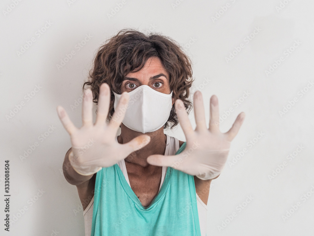 woman social distancing from corona virus covid-19 wearing a protective white face mask and medical gloves holding up hands saying stop woman social distancing from corona virus covid-19 wearing a protective white face mask and medical gloves holding up hands saying stop