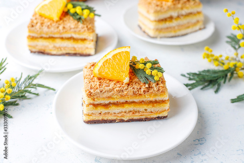 Orange cake decorated with fresh orange slices and mimosa flowers on light background