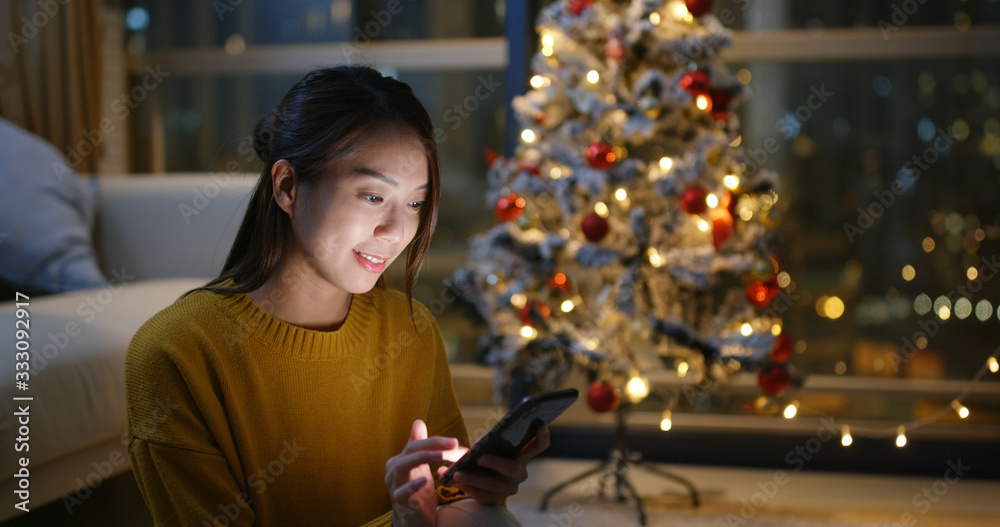 Woman use of cell phone with christmas tree decoration at home Woman use of cell phone with christmas tree decoration at home