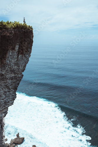 Beautiful girl with long hair on a huge rock overlooking the ocean. Cliff with the waves of the Indian Ocean in Bali. Indonesia. Travels