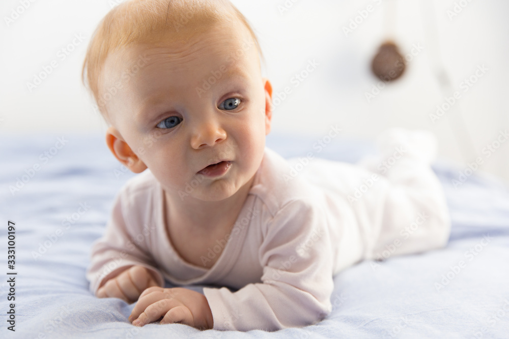 Adorable red-haired baby lying on tummy and looking aside. Close-up portrait of newborn child with blue eyes interested in something. Nursery, newborn kid and infancy concept