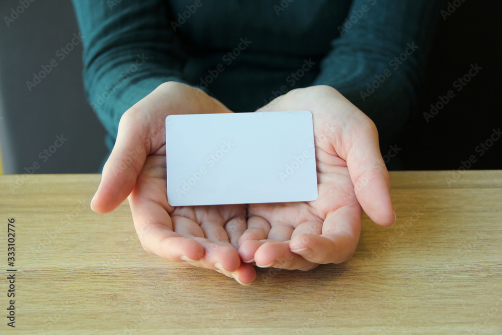 A white rectangular card lies in the opened palms of a girl in a blue sweater. Mockup for design, place for text, copy space A white rectangular card lies in the opened palms of a girl in a blue sweater. Mockup for design, place for text, copy space