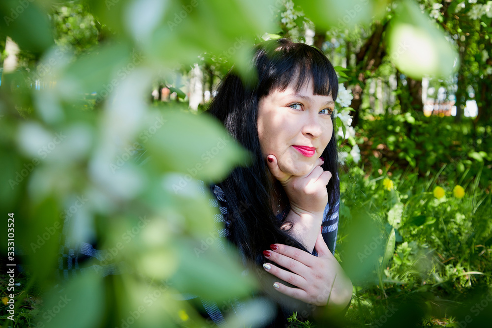 Portrait of an fat chubby plump girl with black hair lying in grass and blossoming apple tree with white flower background in the park in a spring Portrait of an fat chubby plump girl with black hair lying in grass and blossoming apple tree with white flower background in the park in a spring