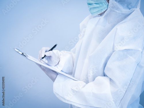 Asian doctor in personal protective suit wearing surgical mask and writing on patient chart, work hard without depression in crisis of covid-19. Medical and healthcare concept.