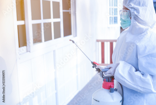 Asian women wear personal protective suits, goggles, masks, and gloves making disinfection and decontamination on a public place. to reduce spreading of disease during crisis covid-19. ...