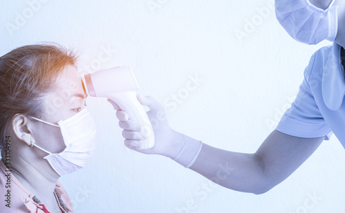 Woman nurse wearing mask and holding medical infrared forehead thermometer to check body temperature for virus symptoms. .Initial screening to prevent the coronavirus outbreak. Healthcare concept.