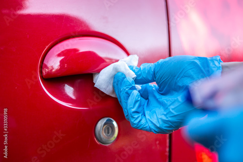 Coronavirus Epidemic Outbreak. Close-up of hand in protective glove using wet wipe to disinfect handle of car doors. 