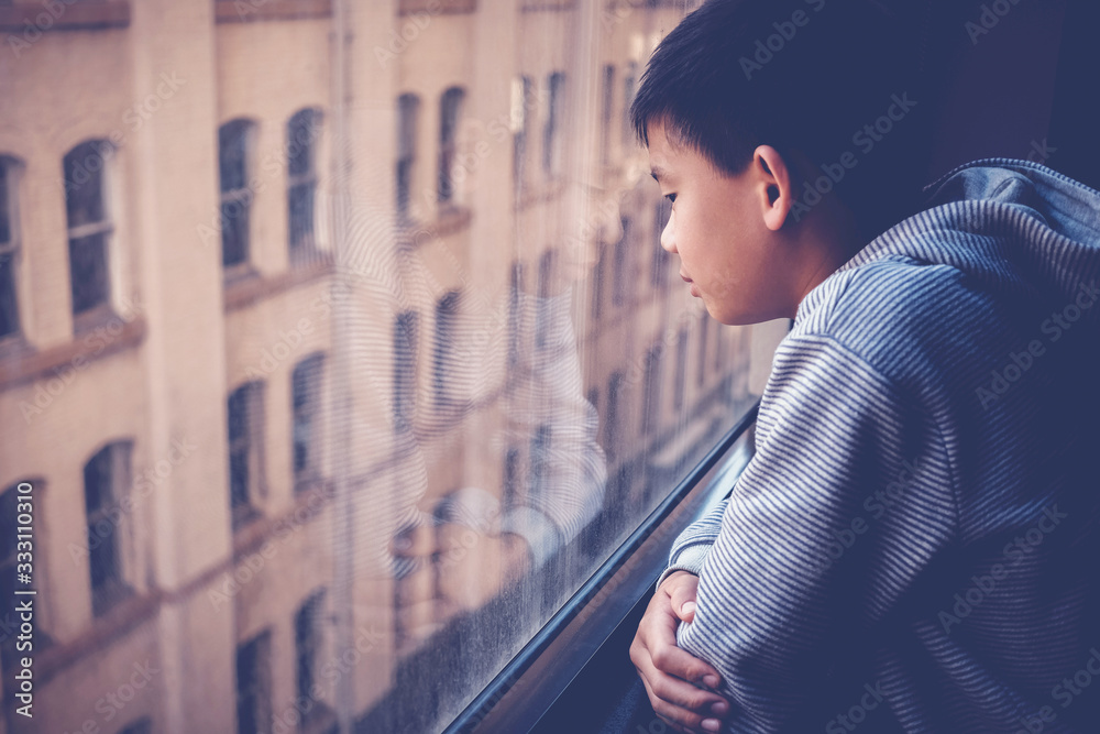 Φωτογραφία Sad Asian preteen boy feeling lonely, looking out of window from his room, socia