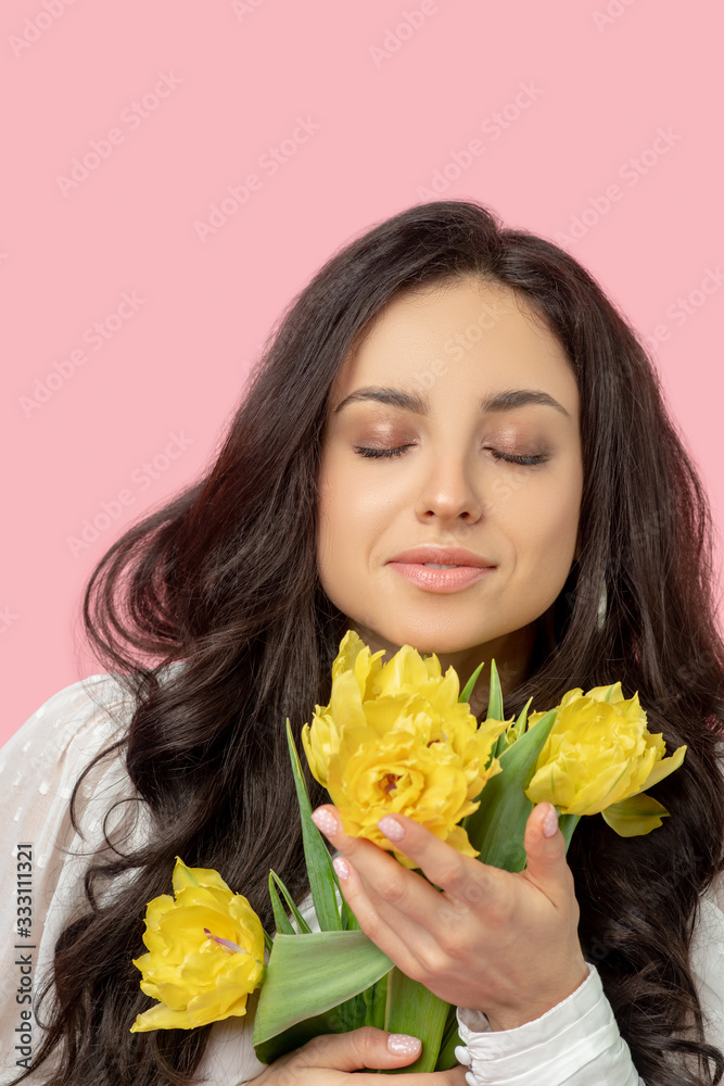 Young pretty dark-haired woman holding yellow flowers and smelling them Young pretty dark-haired woman holding yellow flowers and smelling them