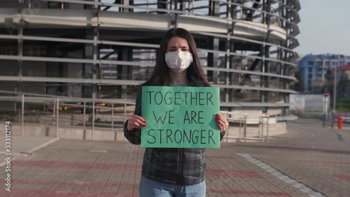 A young woman in a protective mask stands on the street and holds a placard with the inscription together We are stronger. A call for solidarity.