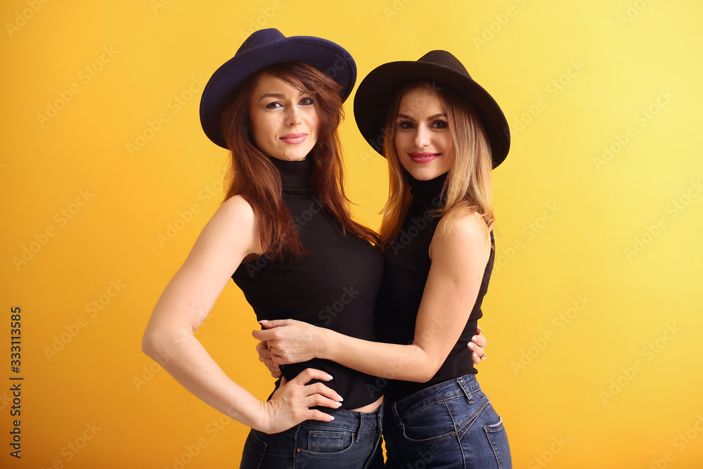 Beautiful girls in a studio. Stylish women on a yellow background. Ladies in a black t-shirt Beautiful girls in a studio. Stylish women on a yellow background. Ladies in a black t-shirt