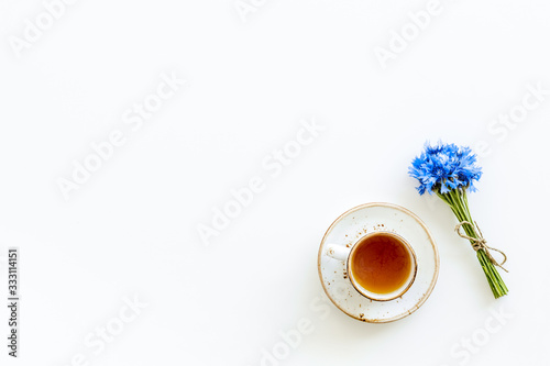 Summer tea party. Cup near cornflowers bouquet on white background top-down copy space