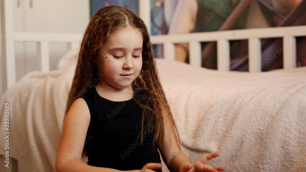 People and music: Liitle pretty girl plays on the african drum in the room at home. She smiles and laugh and do grimaces