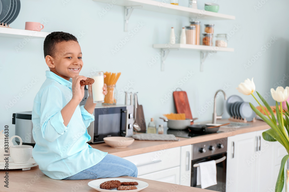 African-American boy drinking milk and eating cookies in kitchen African-American boy drinking milk and eating cookies in kitchen